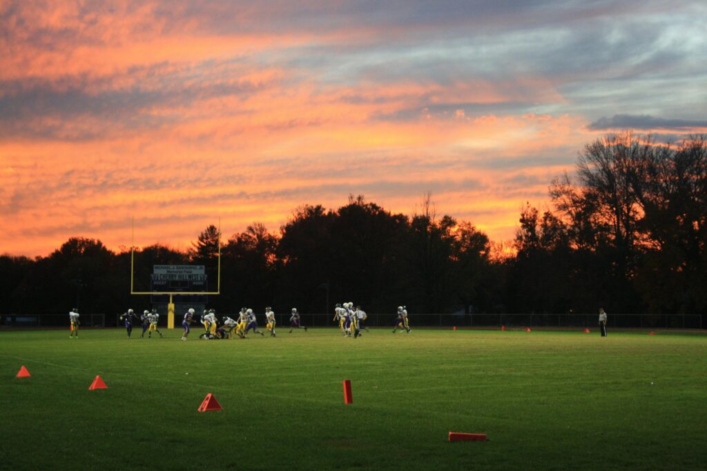 A vibrant sunset backdrop frames a football game on a green field, showcasing teamwork and competition.