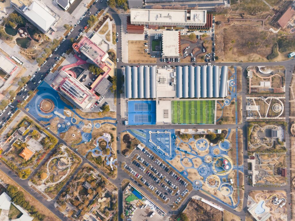 A stunning overhead shot of a sports complex with tennis courts, football field, and nearby park facilities.